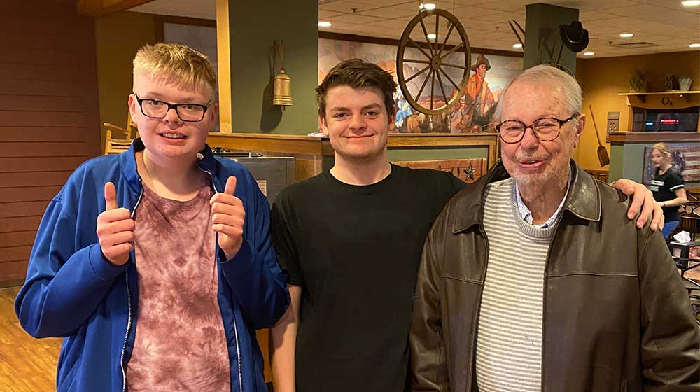 Jack standing with two family members, holding a thumbs up